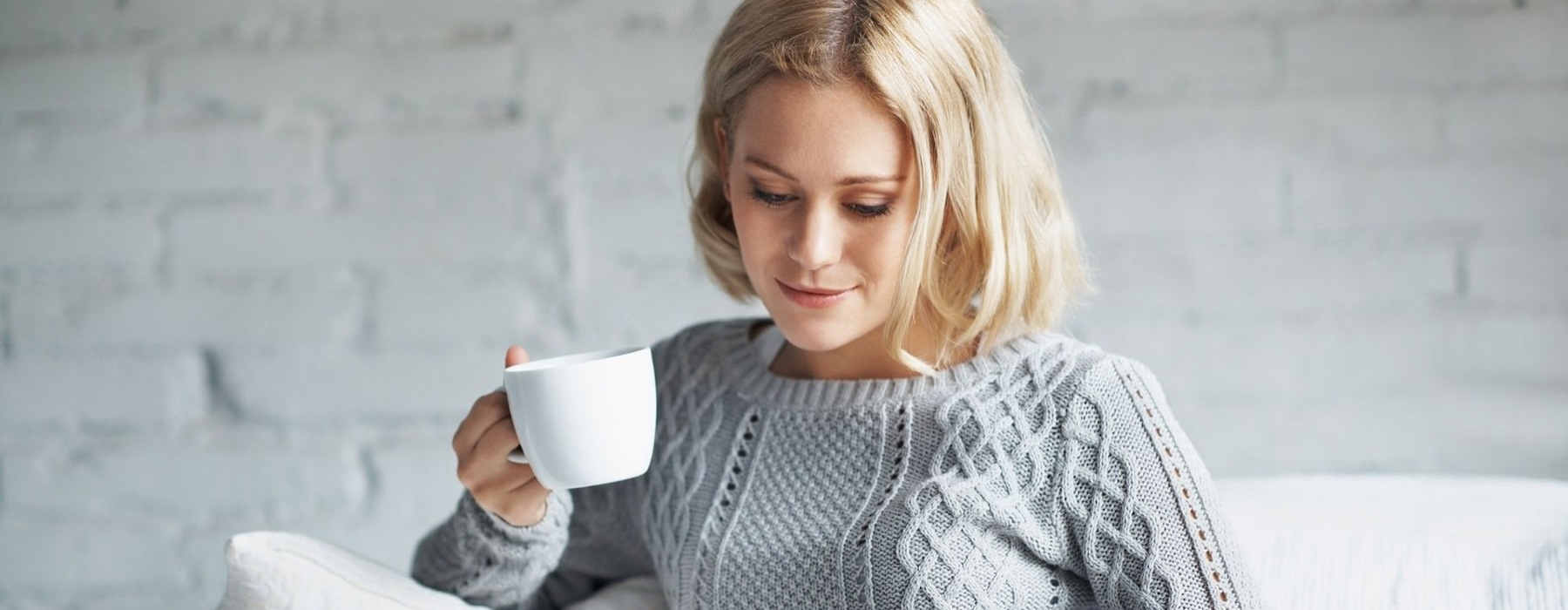 woman sitting down holding a cup looking at a tablet